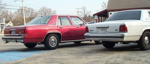 1991 Ford LTD Crown Victoria - Two sedans, one red and one white, are parked next to each other on a paved surface.