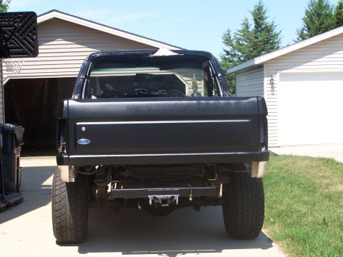1986 Ford Bronco - The rear of a black pickup truck is shown with its tailgate down, parked in front of a garage.