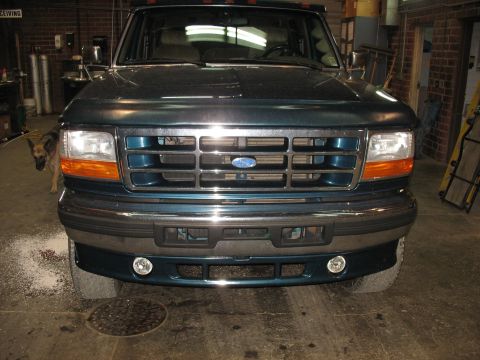 1995 Ford C-350 (Centurion Conversions) - The front grille and headlights of a teal Ford F-Series truck are shown in a garage setting.