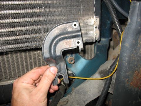 1995 Ford C-350 (Centurion Conversions) - Close-up of a hand holding a black metal bracket near a vehicle's radiator and cooling fins.