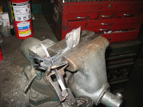 1995 Ford C-350 (Centurion Conversions) - A metal bracket is secured in a vise and being cut with a hacksaw, with a fire extinguisher and tool chest in the background.