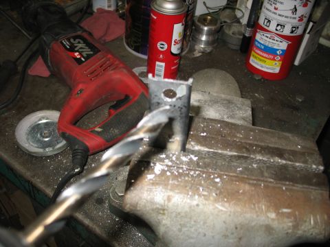 1995 Ford C-350 (Centurion Conversions) - A metal bracket is being drilled while secured in a vise, with a power drill and other tools in the background.