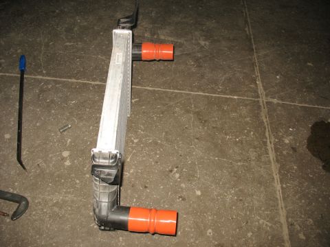 1995 Ford C-350 (Centurion Conversions) - Intercooler part with orange hose fittings, lying on a concrete floor.