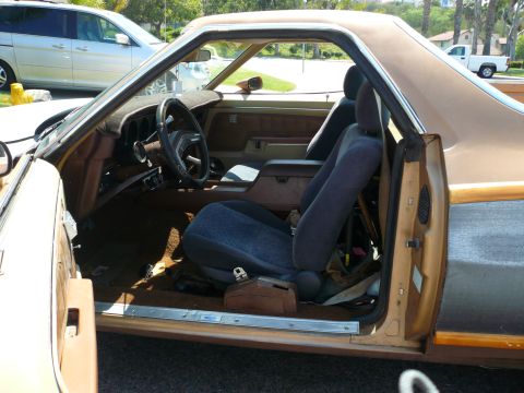 1975 Ford Ranchero - Interior view of a 1975 Ford Ranchero, its brown dashboard, wood-paneled doors, and blue cloth seats.