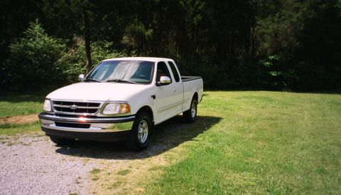 2007 Ford Mustang - A white Ford F-150 pickup truck from the late 1990s is parked outdoors on a sunny day.
