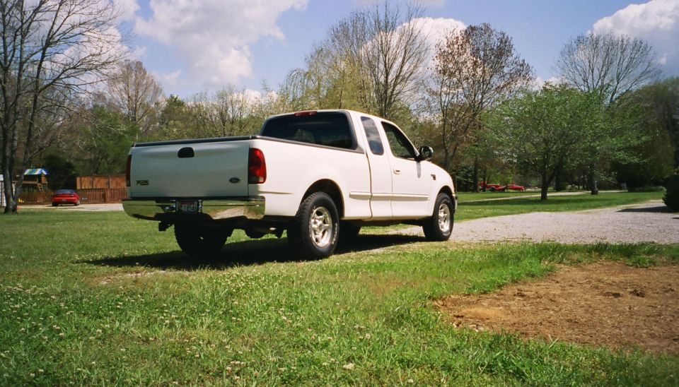 White Ford F-150 SuperCrew pickup truck parked on grass, rear-three-quarter view