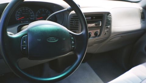 2007 Ford Mustang - Driver's-side interior view of a late-1990s Ford truck showing the dark green airbag steering wheel with cruise-control buttons, the analog…