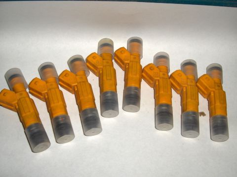 2007 Ford Mustang - A group of yellow fuel injectors are laid out on a white surface.