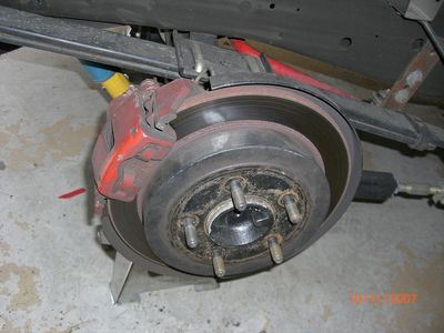 2007 Ford Mustang - Close-up of a 2007 Ford Mustang's rear brake assembly, showing the caliper, rotor, and wheel studs.