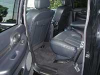 2007 Ford Mustang - Rear passenger compartment of an SUV showing a dark gray leather split bench seat, door panels and floor, photographed through an open rear…