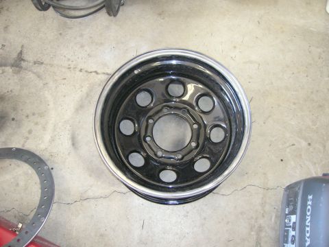 1996 Ford Bronco - A single black steel wheel with a chrome lip is shown from a top-down perspective on a concrete surface.