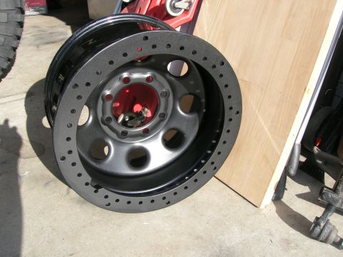 1996 Ford Bronco - A single black aftermarket wheel with a faux beadlock ring is shown resting on a concrete surface.