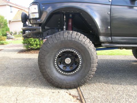 1996 Ford Bronco - Close-up of a modified Ford Bronco's front wheel and fender assembly, highlighting off-road modifications.