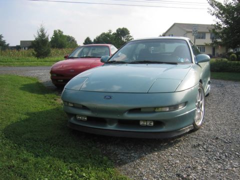 1993 Ford Probe - Two Ford Probes are parked on a gravel driveway next to a grassy lawn.