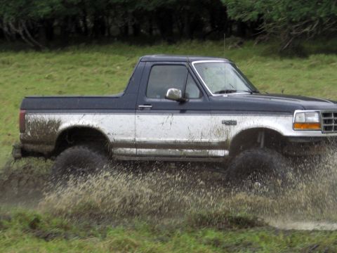 1993 Ford Bronco - This 1993 Ford Bronco is shown kicking up a lot of mud and water as it drives through a wet, grassy field.