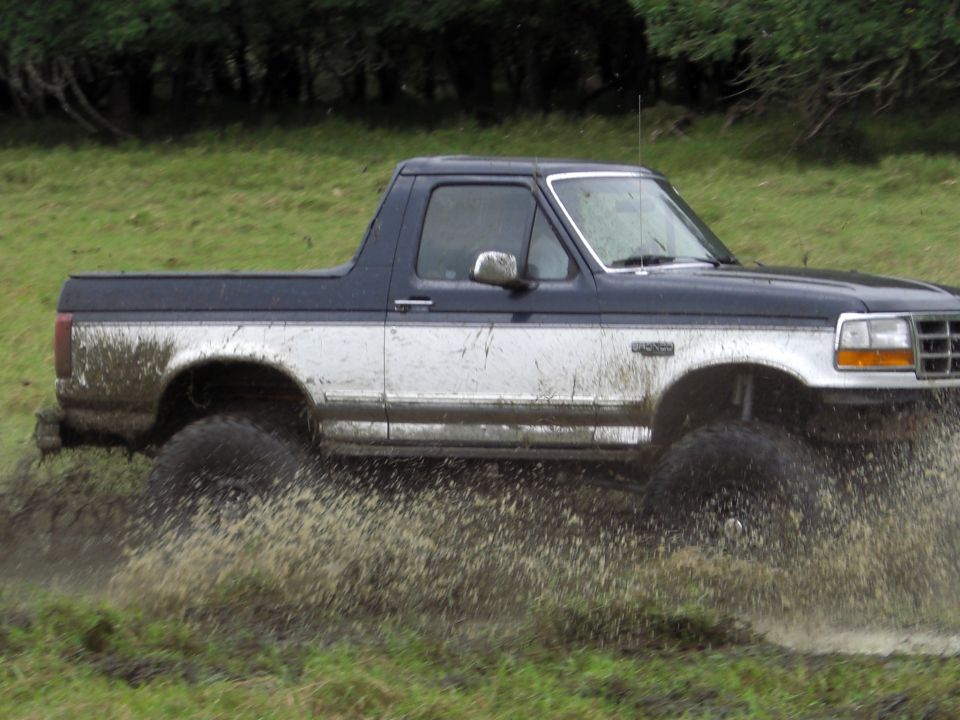 Muddy 1993 Ford Bronco driving through water and splashing