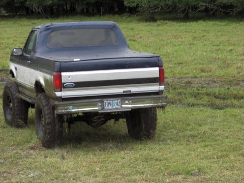 1993 Ford Bronco - This lifted 1993 Ford Bronco features a two-tone paint scheme with a blue soft top and a prominent silver stripe along its rear.