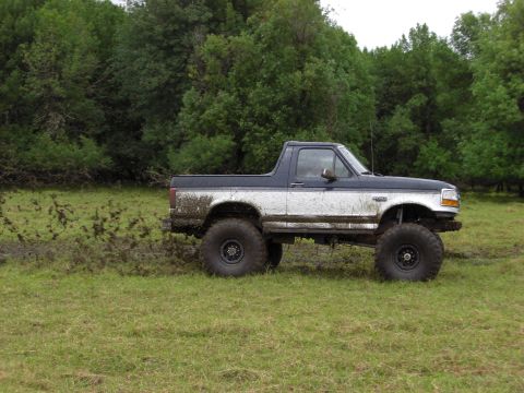 1993 Ford Bronco - This lifted pickup truck is shown off-road with mud splattered on its sides.