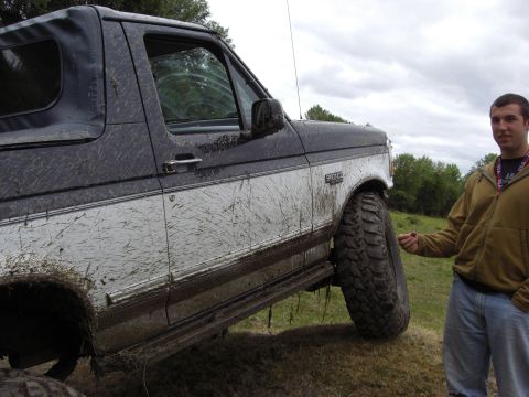 1993 Ford Bronco - A muddy 1993 Ford Bronco is shown off-road, with a man standing beside it and pointing to the large tire.
