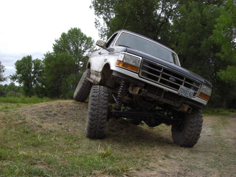 1993 Ford Bronco - A lifted Ford Bronco navigates an off-road obstacle with its front wheels off the ground.