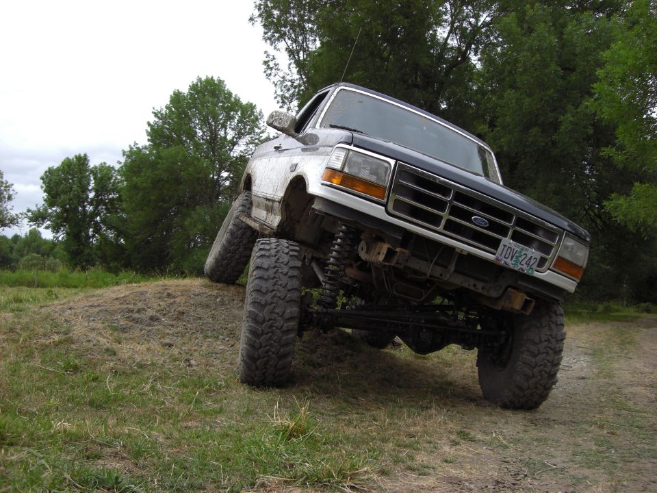 Modified Ford Bronco with large tires climbing a dirt mound