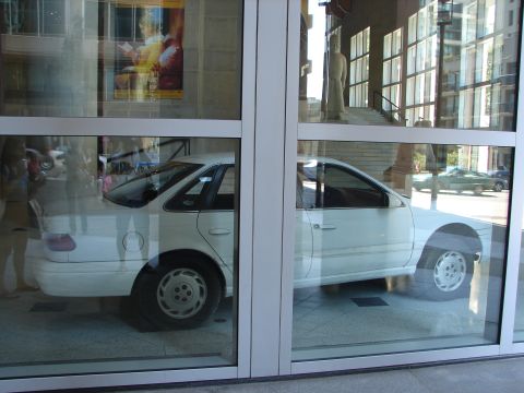 1992 Ford Taurus - A white 1992 Ford Taurus sedan is visible through large glass windows, reflecting the surroundings.