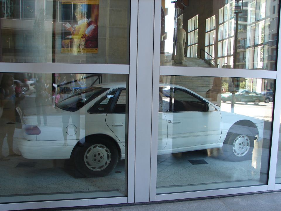 White 1992 Ford Taurus sedan parked behind glass, side view, showing its body shape and wheels