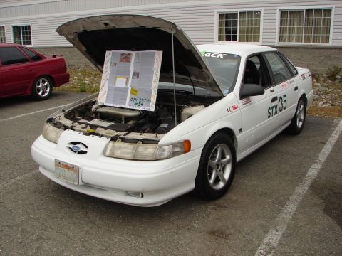 1992 Ford Taurus - A white 1992 Ford Taurus is displayed with its hood open, a newspaper-like display and racing decals.