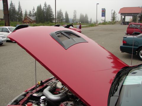 1992 Ford Taurus - A red car with its hood open, revealing the engine and a hood scoop. Other vehicles are visible in the parking lot.