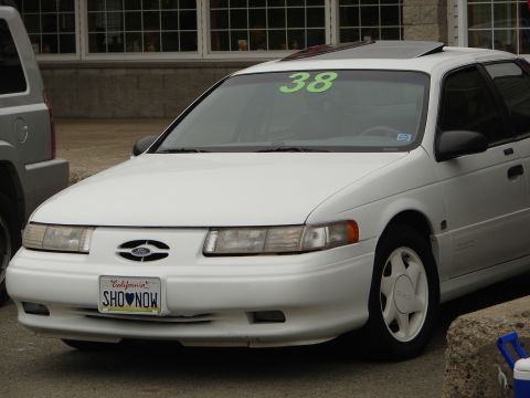 1992 Ford Taurus - White 1992 Ford Taurus seen from the front-right, a sunroof and a California license plate reading 'SHO NOW'.