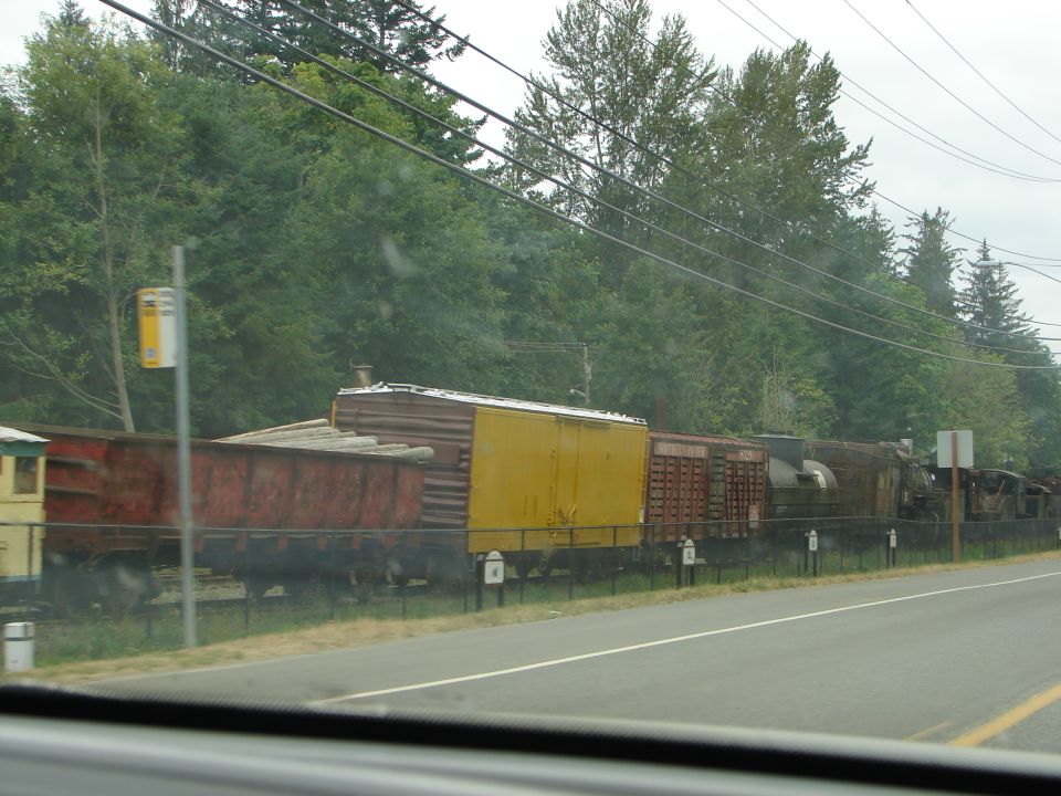 Train cars with yellow and red containers on tracks beside a road