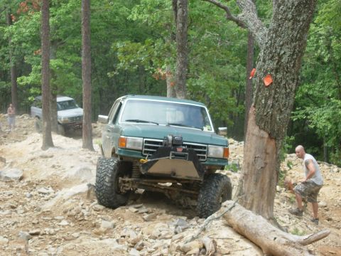 1995 Ford Bronco - A modified green Ford Bronco navigates a challenging off-road course with another vehicle in the background.