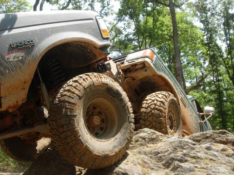 1995 Ford Bronco - Two 4x4s navigate a rocky trail, their off-road capabilities in a forest setting.