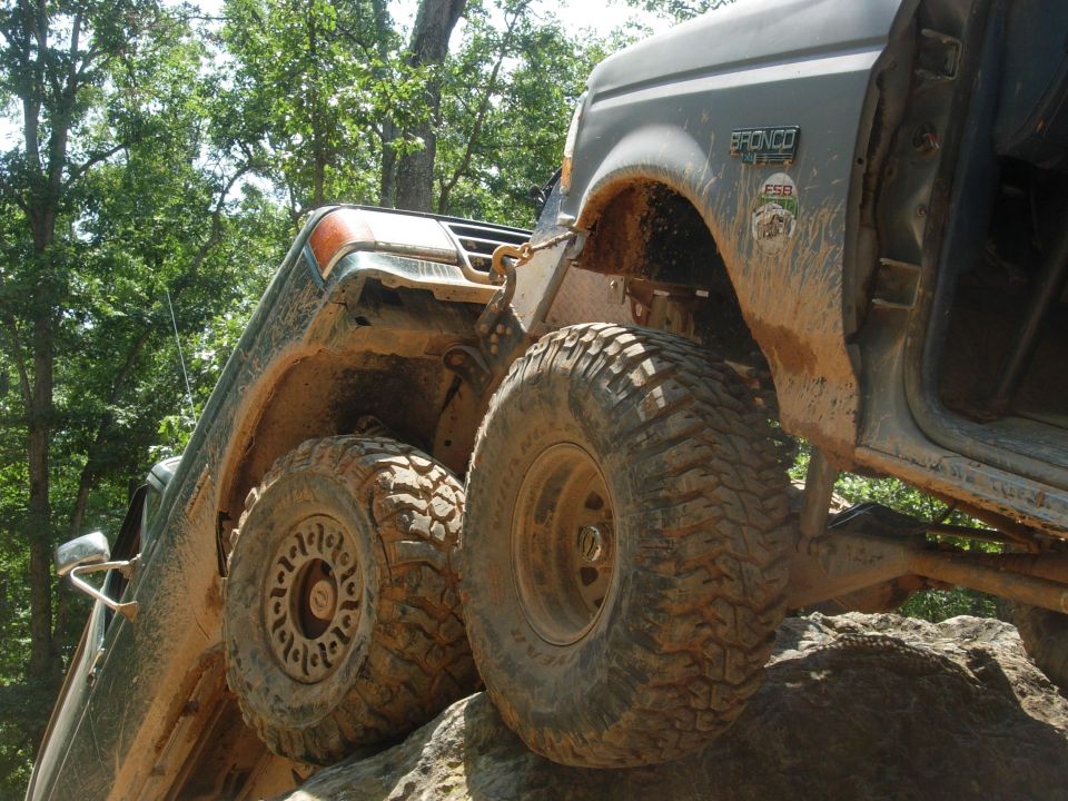 Mud-covered 1995 Ford Bronco with large off-road tires on rocks
