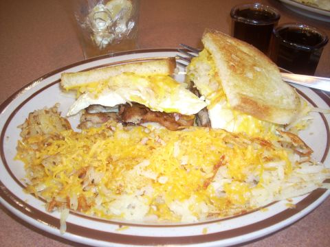 1992 Ford Bronco - A breakfast sandwich with hash browns and cheese is on a plate with two small glasses of dark liquid.