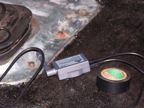 1986 Ford Bronco - A backup camera module and a roll of black tape are visible on a dark, textured surface, possibly inside a vehicle.