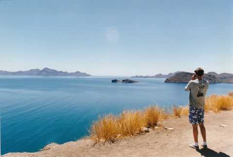 1994 Ford Bronco - A person photographs a scenic bay with islands under a clear blue sky.