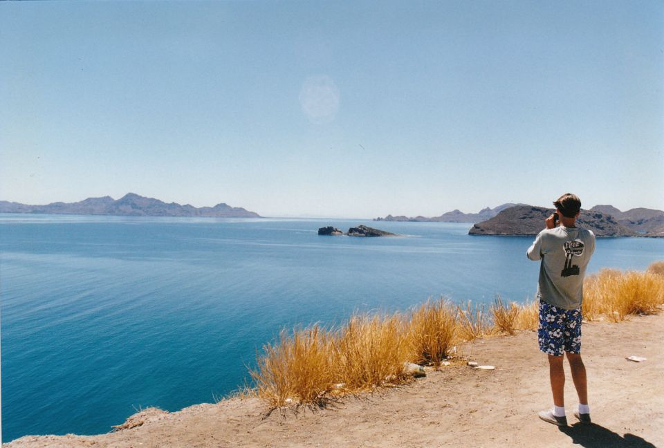 Person stands on a cliff overlooking a bay with islands, taking a photo