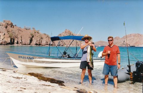 1994 Ford Bronco - Two men proudly display their catch next to a boat named PAISANO on a sunny beach.