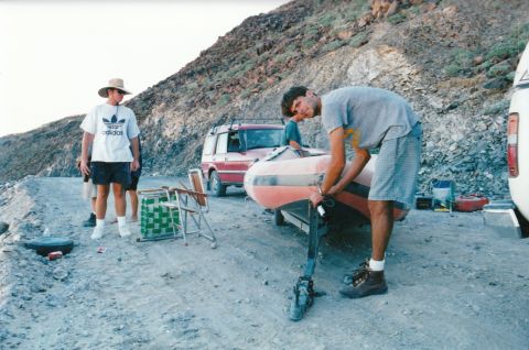 1994 Ford Bronco - A red SUV is parked on a dirt road next to a boat trailer with people around.