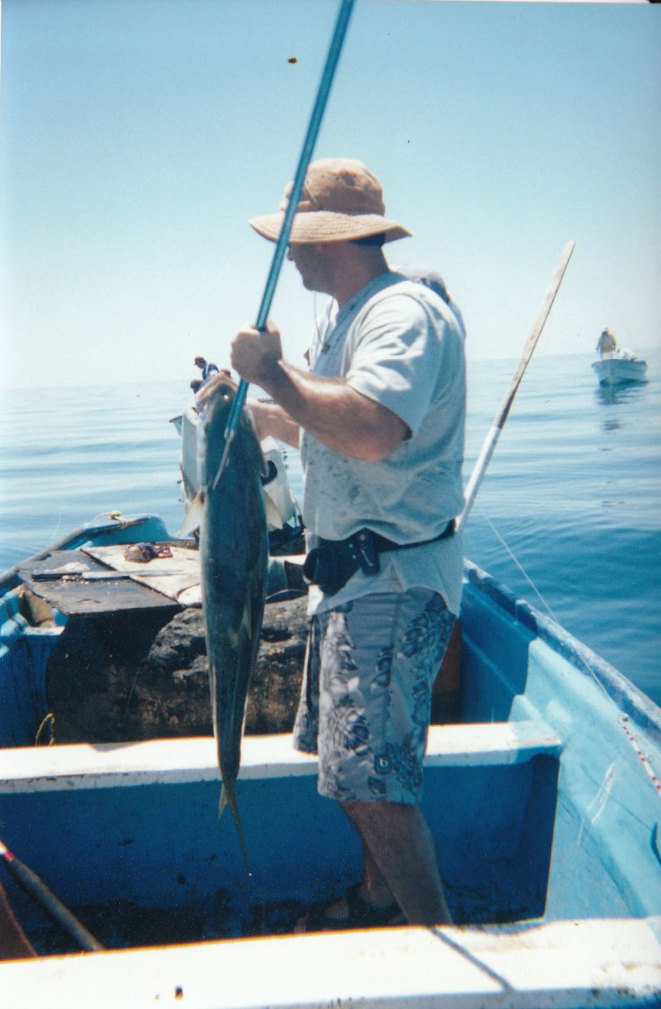 Man on a boat holding a fish he caught. Another boat is in the background