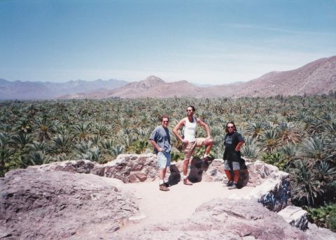 1994 Ford Bronco - Three friends pose for a photo in a scenic desert oasis, with mountains in the distance.