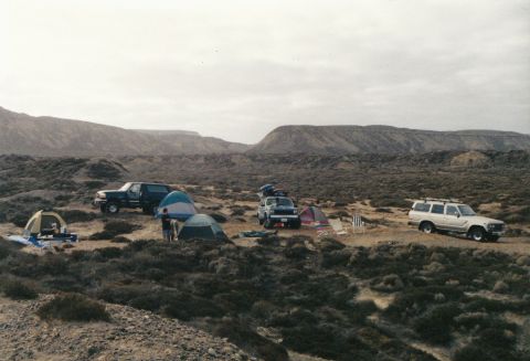 1994 Ford Bronco - Multiple SUVs and tents set up at a desert campsite with hills in the background.