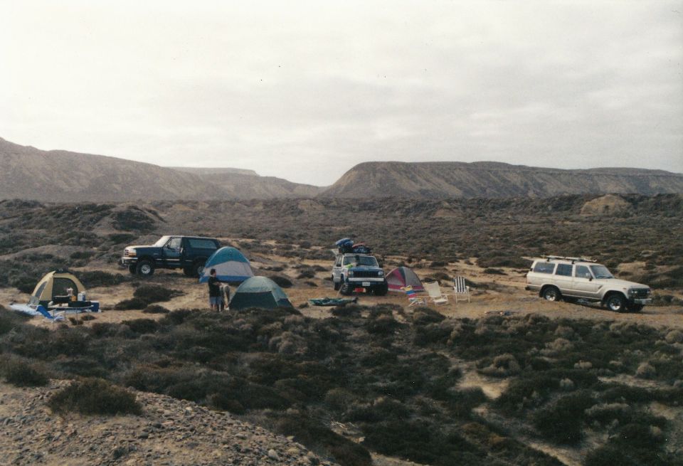 Desert campsite with three SUVs, tents, and chairs under a cloudy sky
