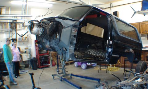 1996 Ford Bronco - The body of a black Ford Bronco is suspended in a workshop, undergoing restoration or repair.