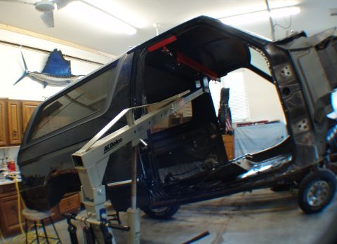 1996 Ford Bronco - A dark blue Ford Bronco body is suspended on a lift, with its doors removed, indicating a restoration project.