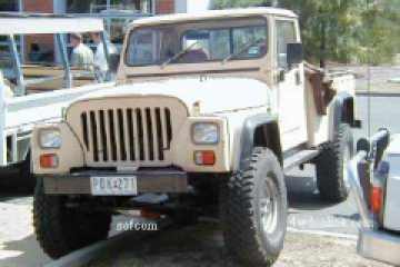 1991 Ford Bronco - Low-resolution driver-side front three-quarter shot of a tan/desert-sand Jeep CJ-8 Scrambler-style pickup with a hardtop cab, slotted grill…