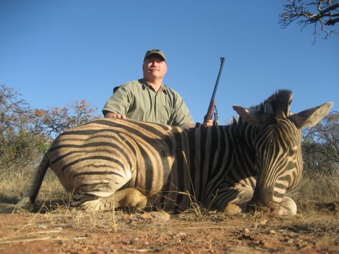 1991 Ford Bronco - A hunter and his downed zebra in a dry, grassy field under a clear blue sky.