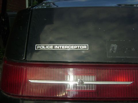 1981 Ford Mustang - The rear of a black vehicle displays a "POLICE INTERCEPTOR" badge and a red taillight.