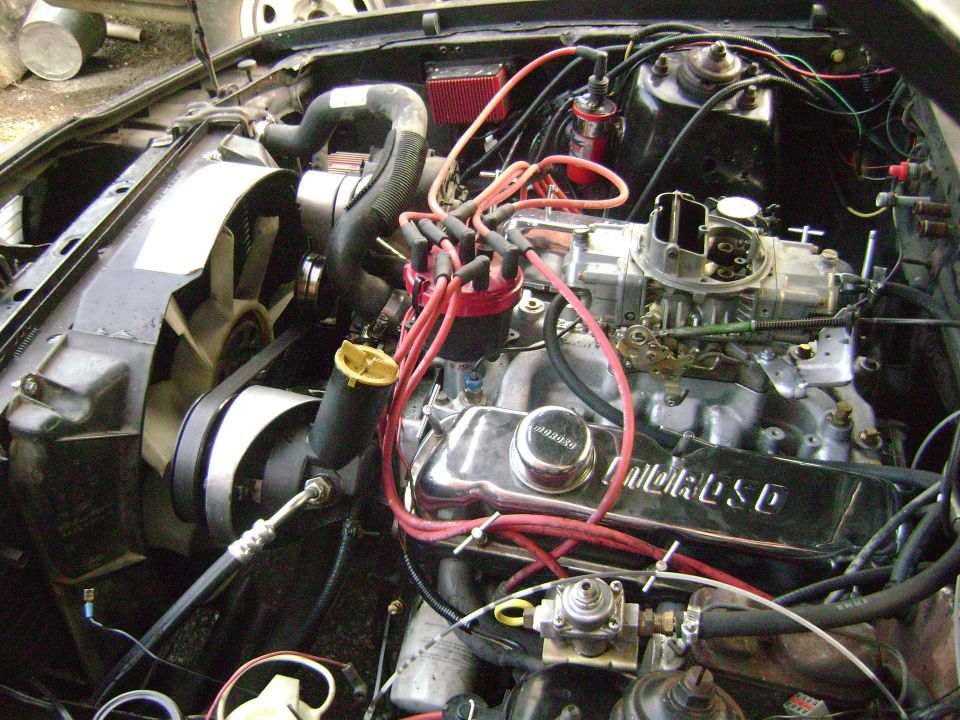 Engine bay with V8 engine, carburetor, distributor, and fan visible. Supermotors.net logo in lower right
